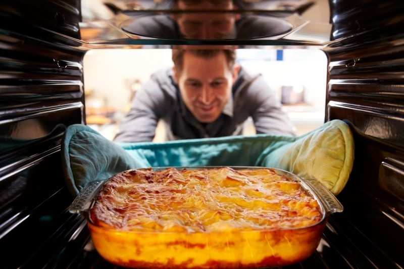 man looking at a lasagna in the oven